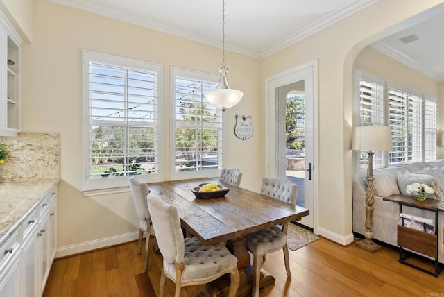 dining room with plenty of natural light, light wood-style flooring, ornamental molding, and arched walkways