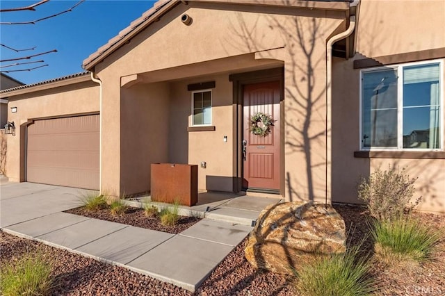 entrance to property with a garage, driveway, a tile roof, and stucco siding