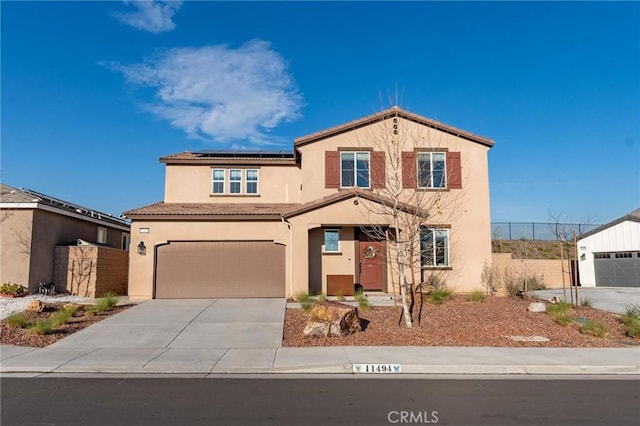 mediterranean / spanish home featuring stucco siding, fence, concrete driveway, solar panels, and a tiled roof