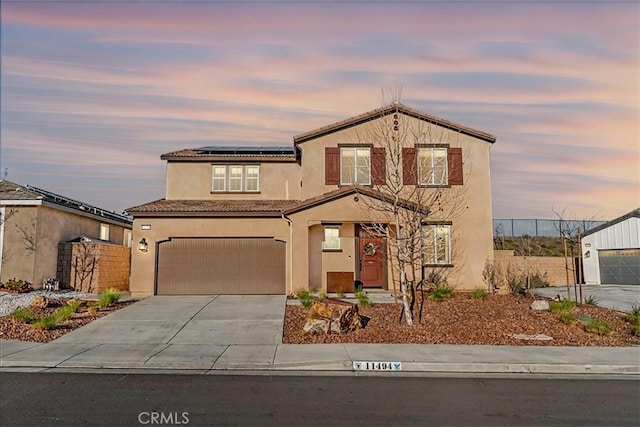 view of front of home featuring stucco siding, fence, concrete driveway, solar panels, and a tiled roof