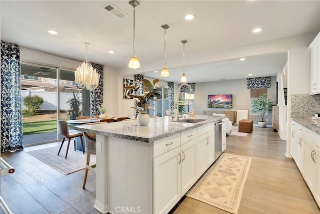 kitchen with an island with sink, light stone counters, pendant lighting, sink, and white cabinetry