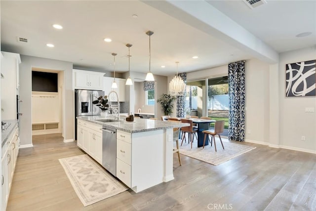 kitchen featuring white cabinetry, stainless steel appliances, light stone counters, and a kitchen island with sink