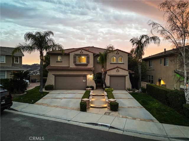 mediterranean / spanish house with driveway, an attached garage, a tiled roof, and stucco siding