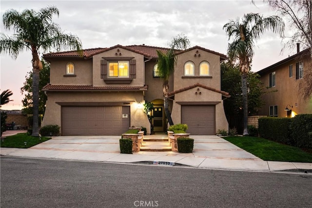 mediterranean / spanish house with a garage, concrete driveway, a tile roof, and stucco siding