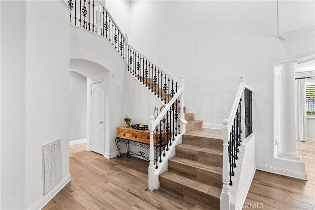 staircase with decorative columns, a high ceiling, visible vents, and wood finished floors