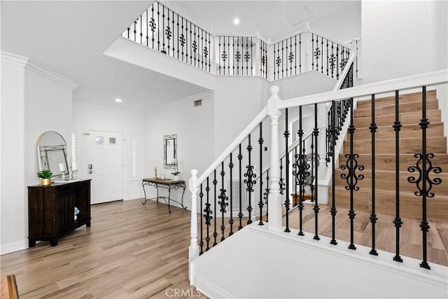 staircase featuring baseboards, ornamental molding, wood finished floors, a high ceiling, and recessed lighting