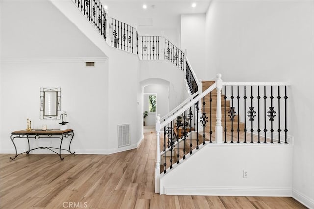 stairs featuring visible vents, a towering ceiling, baseboards, and wood finished floors