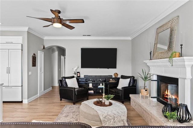 living area with arched walkways, a premium fireplace, wood finished floors, baseboards, and ornamental molding