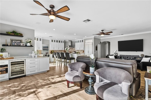 living room with light wood-style flooring, wine cooler, arched walkways, and ornamental molding