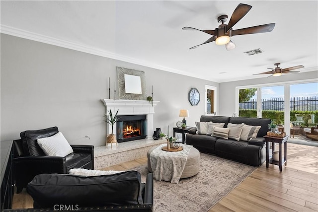 living area featuring visible vents, a ceiling fan, a premium fireplace, wood finished floors, and crown molding