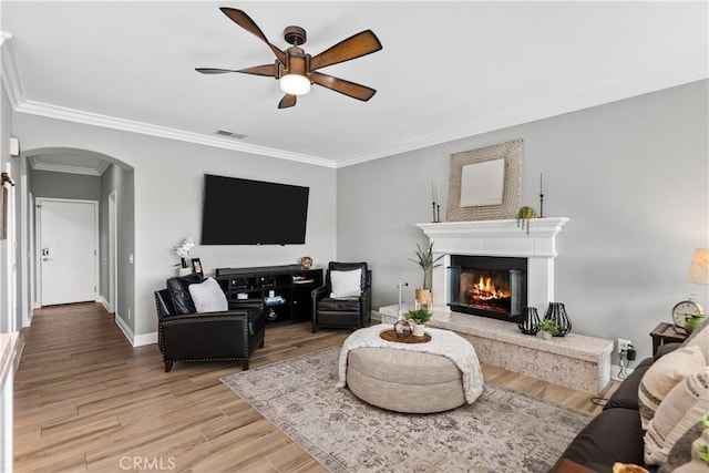 living room featuring arched walkways, crown molding, visible vents, ceiling fan, and light wood-type flooring