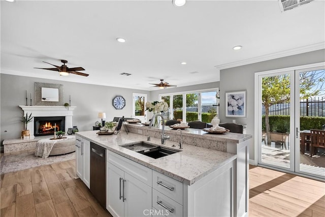 kitchen with ornamental molding, open floor plan, a sink, a kitchen island with sink, and stainless steel dishwasher