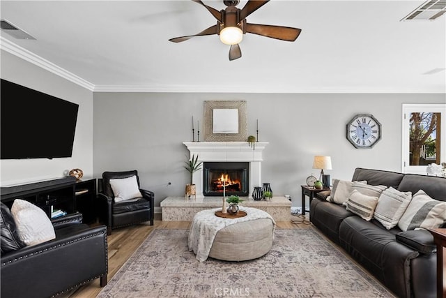 living area with a warm lit fireplace, wood finished floors, visible vents, and crown molding