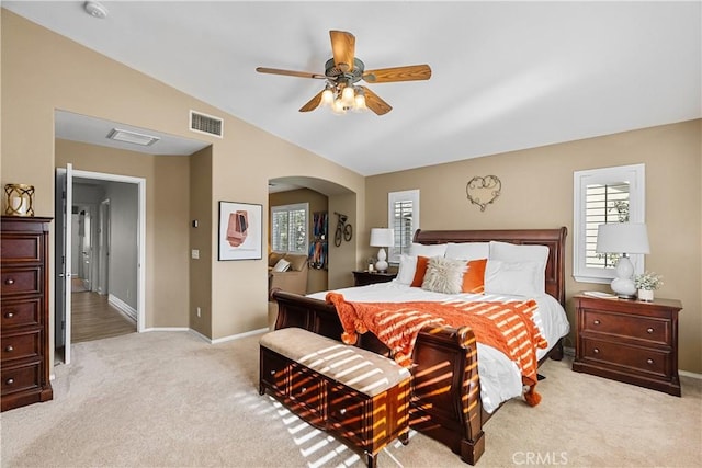 bedroom with lofted ceiling, arched walkways, light colored carpet, visible vents, and baseboards