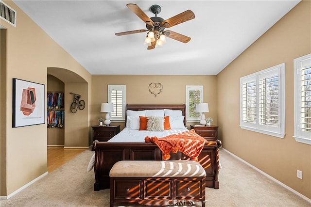 bedroom featuring arched walkways, lofted ceiling, light colored carpet, visible vents, and baseboards