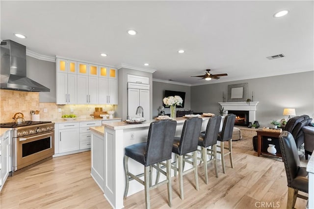 kitchen with visible vents, a kitchen breakfast bar, high end stainless steel range oven, light countertops, and wall chimney range hood