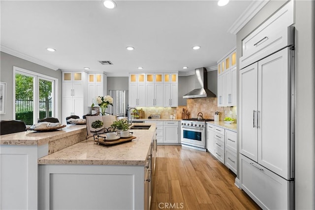 kitchen with premium appliances, a center island with sink, visible vents, a sink, and wall chimney range hood