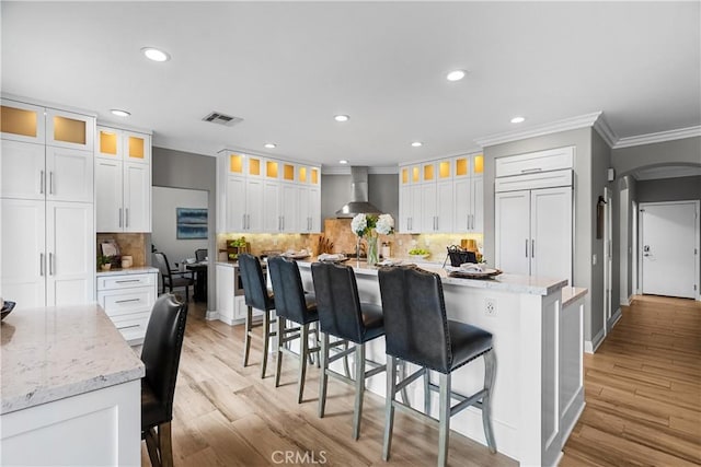 kitchen featuring wall chimney exhaust hood, arched walkways, white cabinets, and a breakfast bar area