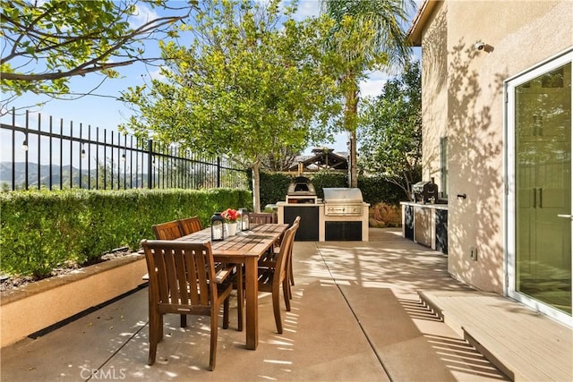 view of patio / terrace with exterior kitchen, outdoor dining area, a grill, and a fenced backyard