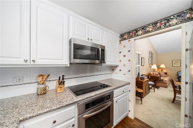 kitchen featuring white cabinetry, lofted ceiling, stainless steel appliances, light stone countertops, and backsplash