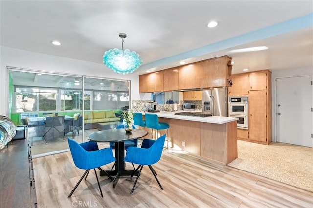 kitchen featuring open floor plan, decorative light fixtures, a peninsula, stainless steel appliances, and light countertops