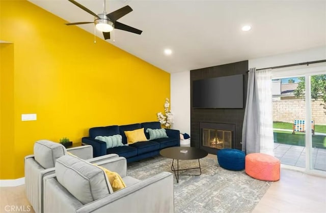 living room featuring ceiling fan, a large fireplace, vaulted ceiling, and light hardwood / wood-style floors