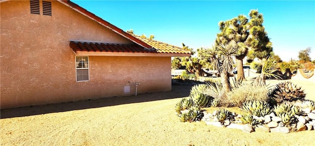 view of side of home with stucco siding and a tiled roof