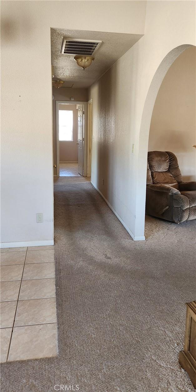 hall with carpet, baseboards, arched walkways, visible vents, and a textured ceiling