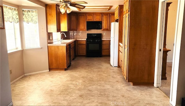 kitchen with light countertops, black appliances, decorative backsplash, a sink, and brown cabinetry