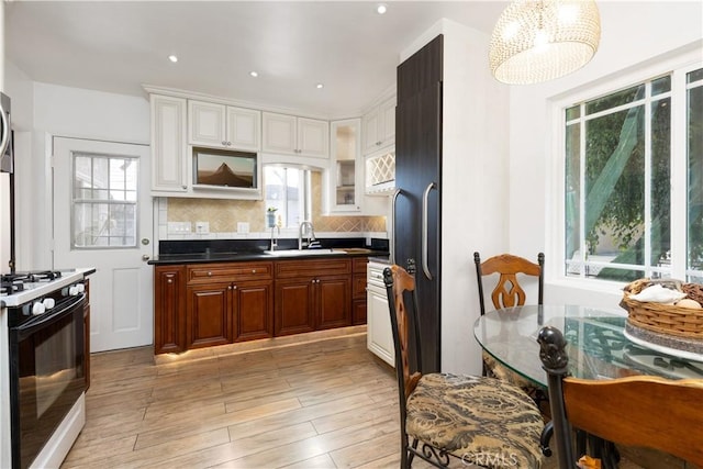 kitchen with gas range oven, decorative backsplash, white cabinetry, a sink, and light wood-type flooring