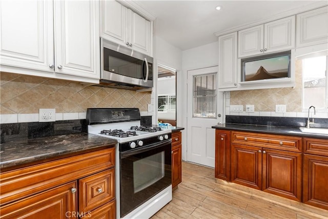 kitchen with light wood-style flooring, stainless steel microwave, a sink, white cabinets, and gas range oven