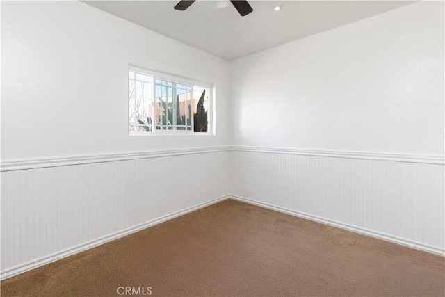 carpeted spare room with a wainscoted wall and ceiling fan