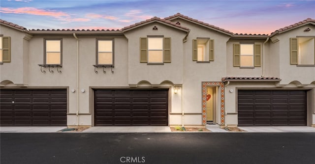 view of front of property with an attached garage, driveway, a tiled roof, and stucco siding