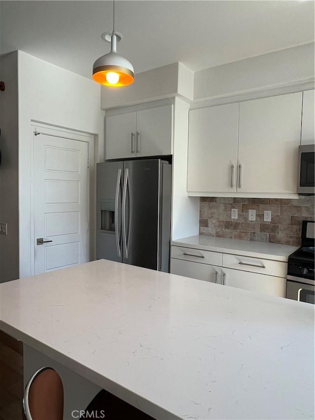 kitchen featuring light stone counters, stainless steel appliances, white cabinets, decorative backsplash, and decorative light fixtures