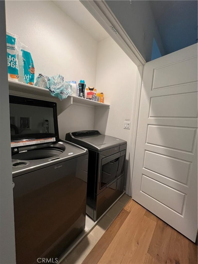 clothes washing area with laundry area, washer and clothes dryer, and light wood-style floors