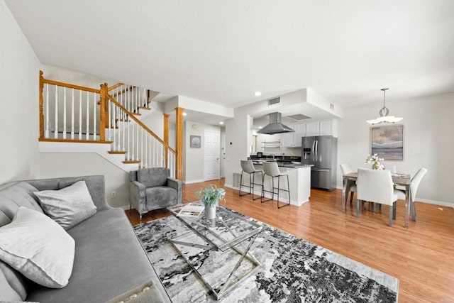 living area featuring recessed lighting, visible vents, light wood-style flooring, stairway, and baseboards