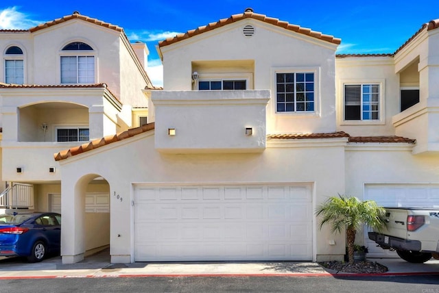 mediterranean / spanish house with a tiled roof, an attached garage, and stucco siding