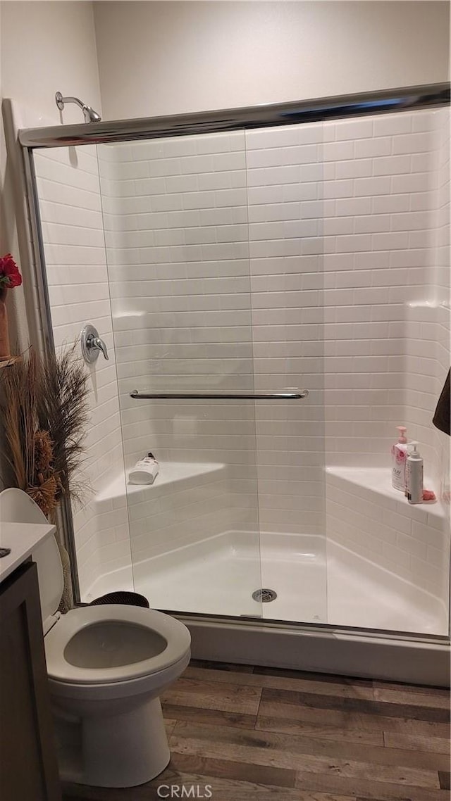 bathroom featuring toilet, hardwood / wood-style flooring, a shower with shower door, and vanity