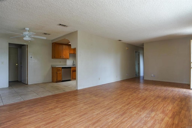 unfurnished living room with sink, ceiling fan, light wood-type flooring, and a textured ceiling