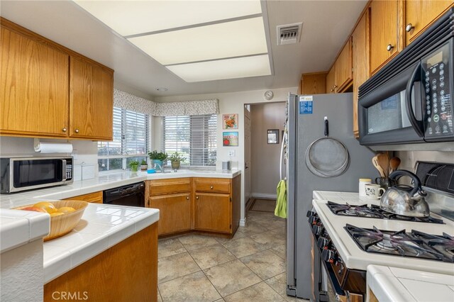 kitchen featuring visible vents, tile counters, brown cabinets, light tile patterned flooring, and black appliances