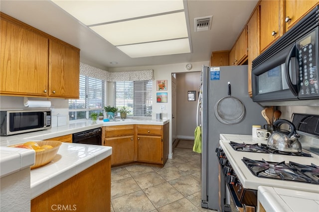 kitchen with tile countertops, black appliances, brown cabinetry, light tile patterned floors, and visible vents