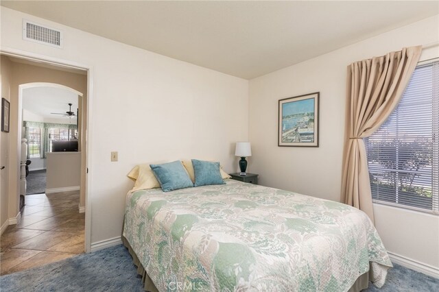 carpeted bedroom with visible vents, arched walkways, baseboards, and tile patterned flooring