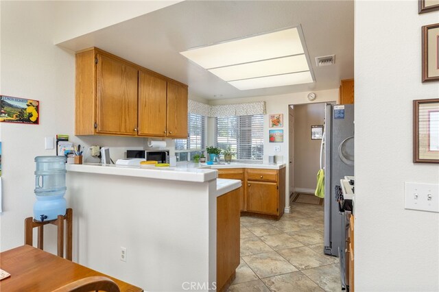 kitchen with visible vents, brown cabinets, a peninsula, appliances with stainless steel finishes, and light countertops