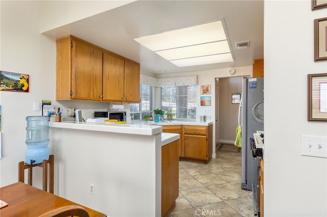 kitchen with a peninsula, visible vents, brown cabinetry, light countertops, and appliances with stainless steel finishes