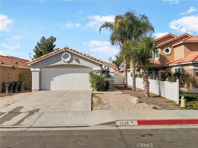 mediterranean / spanish home featuring stucco siding, concrete driveway, fence, a garage, and a tiled roof