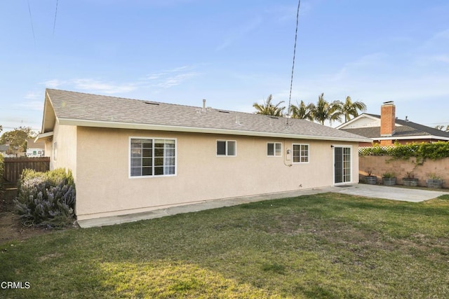 rear view of property with a patio, roof with shingles, fence, a yard, and stucco siding