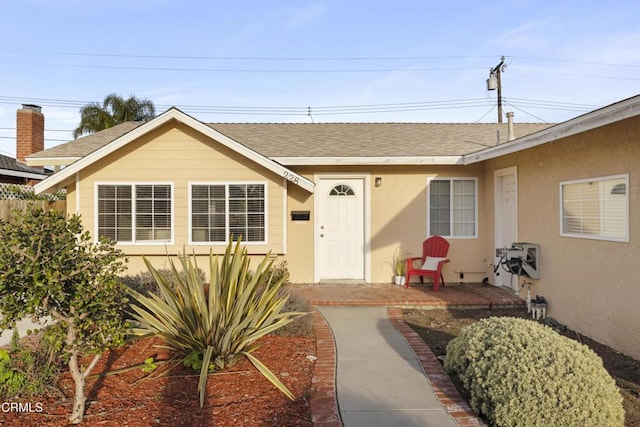 entrance to property featuring a shingled roof, a patio, and stucco siding