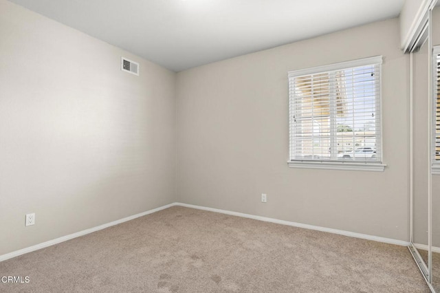 empty room with baseboards, visible vents, and light colored carpet