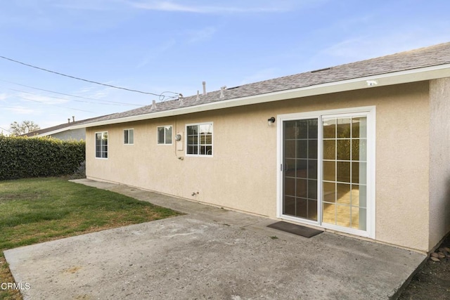 rear view of house featuring a shingled roof, a patio, a lawn, and stucco siding