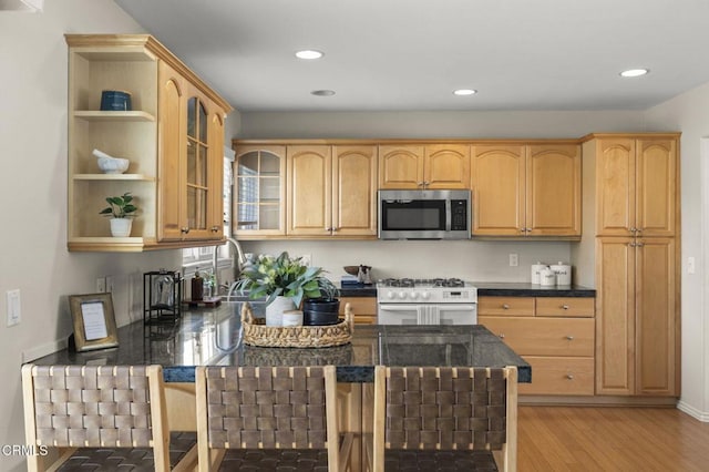 kitchen with white gas range, open shelves, stainless steel microwave, dark countertops, and glass insert cabinets